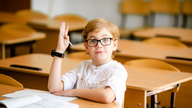 Cute blonde school student with stylish glasses writing in classroom