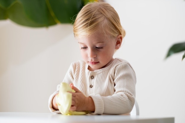 Cute blonde serious girltoddler two or three year old playing with yellow sticky slime indoors on wh