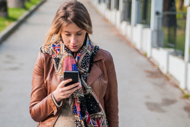 Cute blonde talking on a cell phone. Pretty young Caucasian woman speaking on the phone outdoors in park