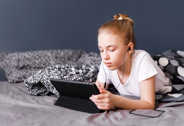 Cute blonde teen girl watching video on tablet on the bed