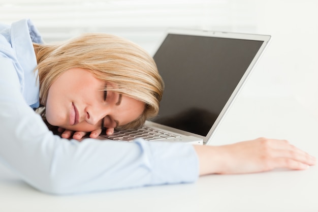 Cute blonde woman sleeping on her notebook holding cup of coffee