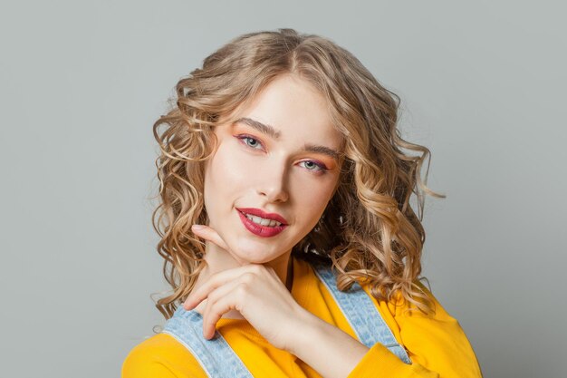 Cute blonde woman smiling on gray background