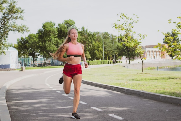 Cute blondy sporty woman with long hair is jogging in the park