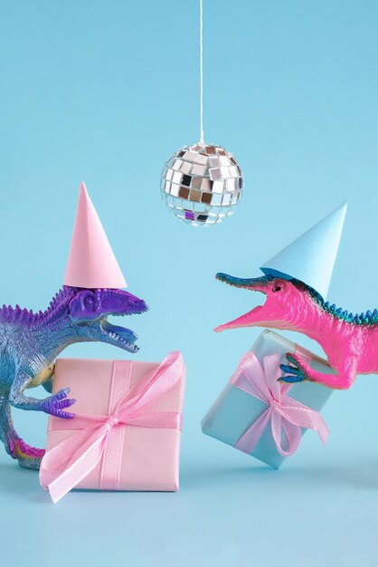 Foto dinosauri blu e rosa carini che indossano un cappello da festa e tengono in mano una scatola di regali sullo sfondo blu