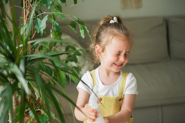 Carina ragazza dai capelli ricci con gli occhi azzurri di 4 anni versa le piante d'appartamento con l'acqua da un annaffiatoio in una casa accogliente il bambino aiuta sua madre con le faccende domestiche ecofriendly planet nature