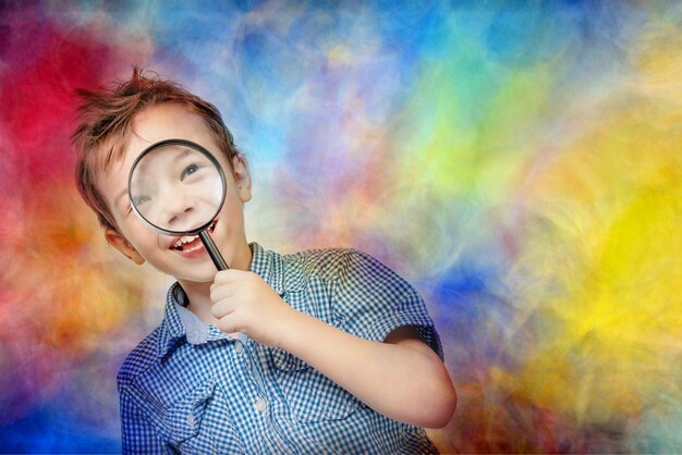 Foto ragazzo carino in una camicia blu che guarda attraverso una lente d'ingrandimento su uno sfondo colorato