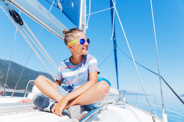 Cute boy on board of sailing yacht on summer cruise. Travel adventure, yachting with child on family vacation. Kid clothing in sailor style, nautical fashion.