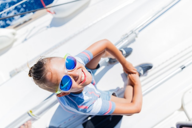 Ragazzo carino a bordo di yacht a vela in crociera estiva. avventura di viaggio, yachting con bambino in vacanza in famiglia. abbigliamento bambino in stile marinaio, moda nautica.