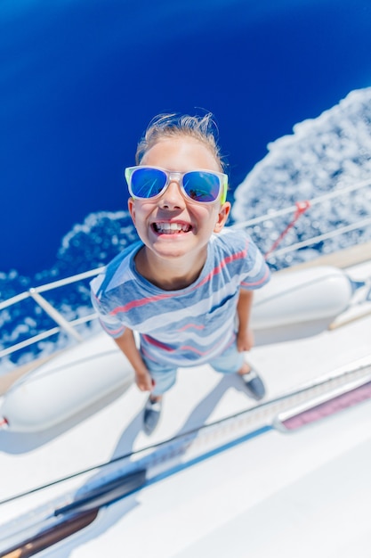 Cute boy on board of sailing yacht on summer cruise. Travel adventure, yachting with child on family vacation. Kid clothing in sailor style, nautical fashion.