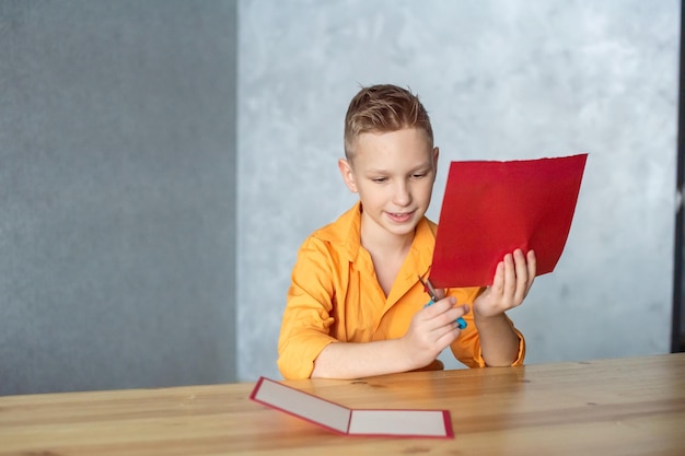 Cute boy carves a heart out of red colored paper for a Valentine's Day card