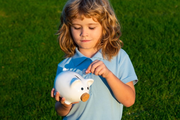 Cute boy collecting money to piggy bank. Little child boy with piggy bank outdoor. Kid hold piggybank. Money cash and investment.