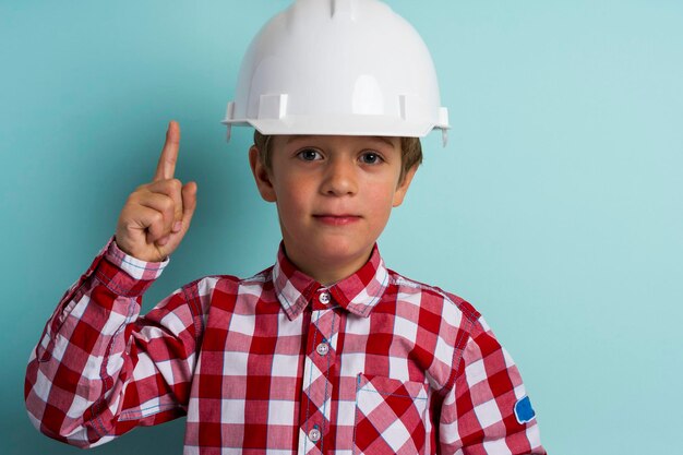 Un ragazzo carino in un casco da costruzione protegge la sua testa, un ritratto di un piccolo costruttore in un casco