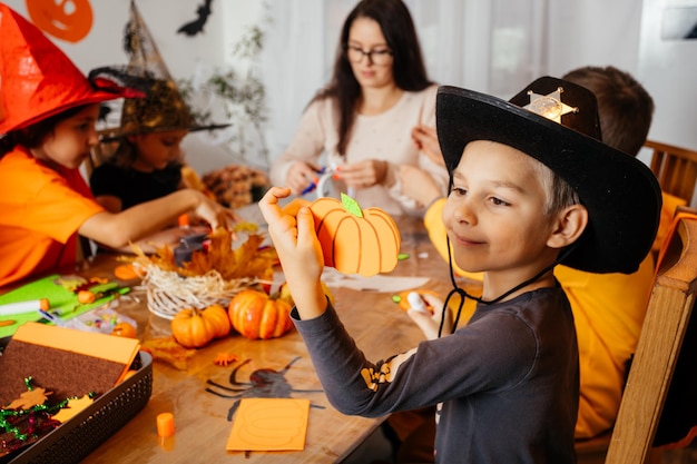 Cute boy in cowboy hat demonstrates his handmade paper pumpkin