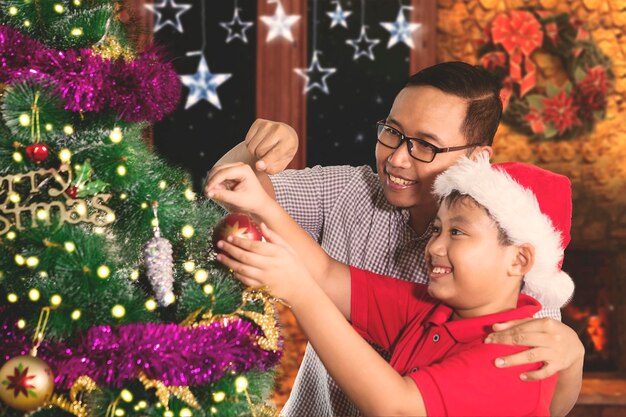 Cute boy decorating Christmas tree with his father