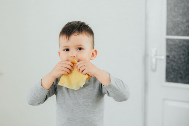 Cute boy eating delicious pancakes sitting at a table on a light background