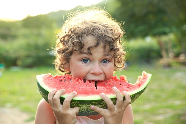 写真 カメラで熟したスイカを食べるかわいい男の子