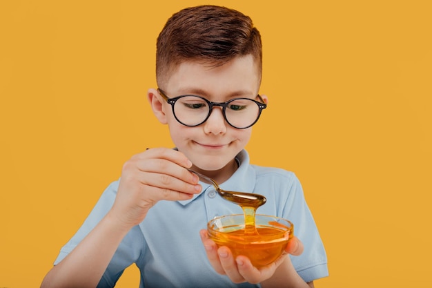 Cute boy eating sweet honey in glasses smiling while enjoying healthy sweet honey against yellow