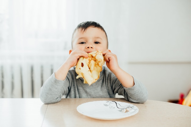 Cute boy eats pancakes at the table playfully and fun