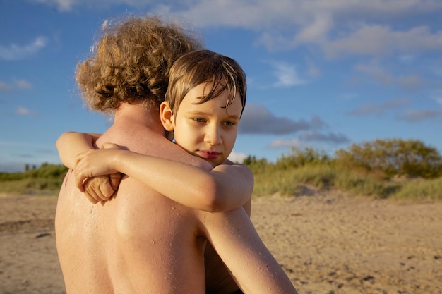 Photo cute boy embracing shirtless father at beach against sky