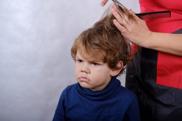 Aspetto europeo ragazzo carino durante il taglio di capelli con le forbici