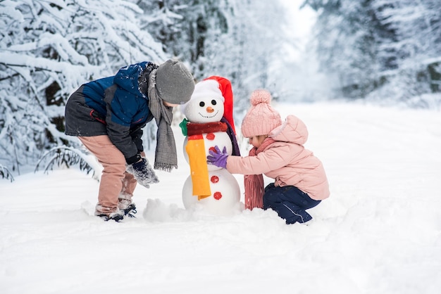 Ragazzo sveglio e ragazza che costruiscono pupazzo di neve nella foresta bianca di inverno