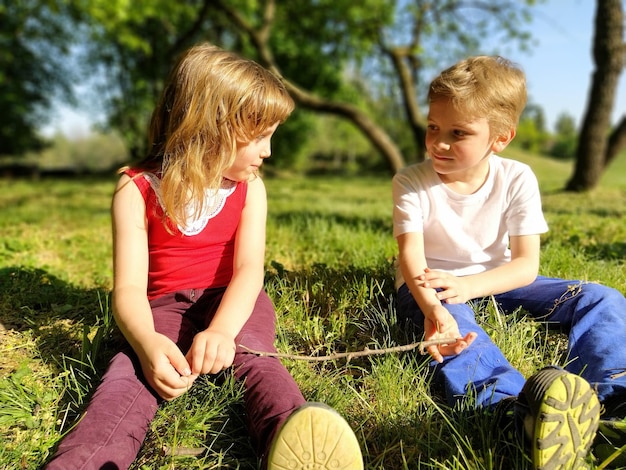 Cute boy and girl with blond hair are sitting on the grass and looking at each other Kids