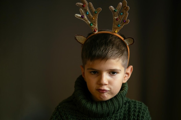 A cute boy in green sweater and antlers makes face