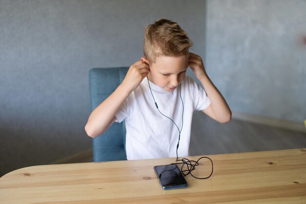 かわいい男の子が有線ヘッドホンを携帯電話に接続して音楽を聴いています