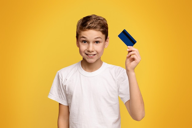Cute boy holding credit card orange studio background