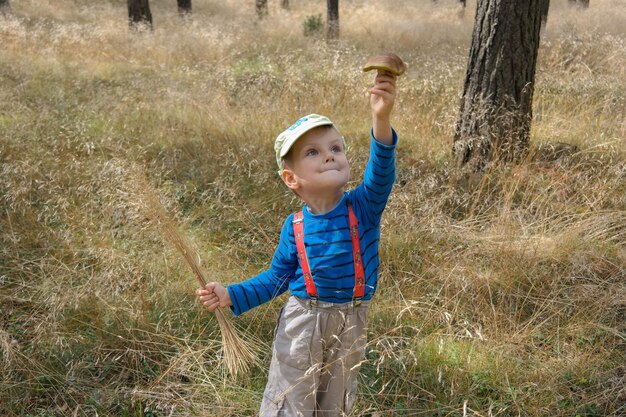 Photo cute boy holding mushroom while standing on field