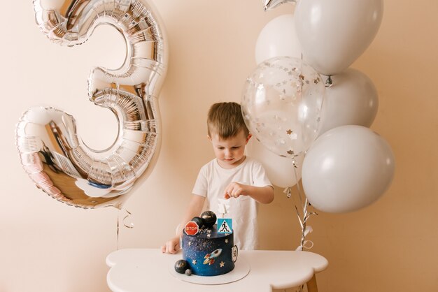 Cute boy is celebrating his birthday and eating a delicious beautiful cake, photo of a child with balloons