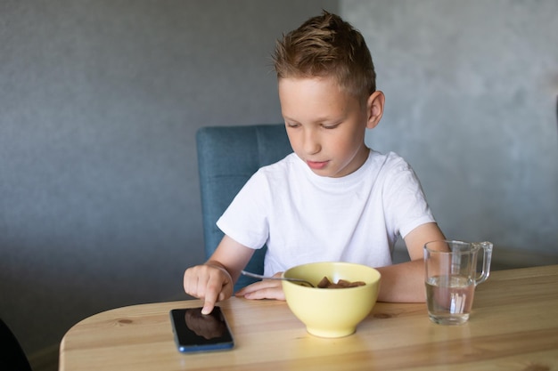 A cute boy is having breakfast and looking at the phone A glass of water