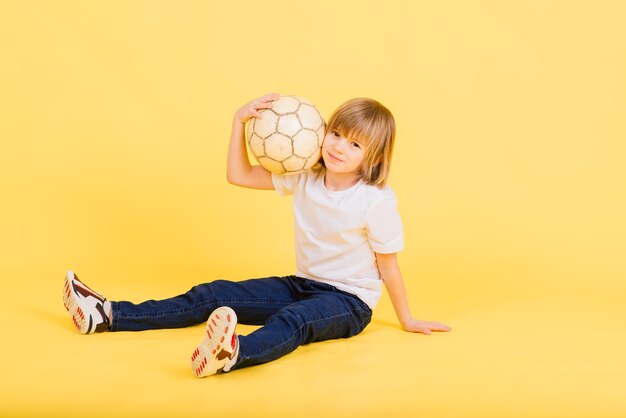 かわいい男の子は、黄色に分離された本革で作られたサッカー ボールを持っています。