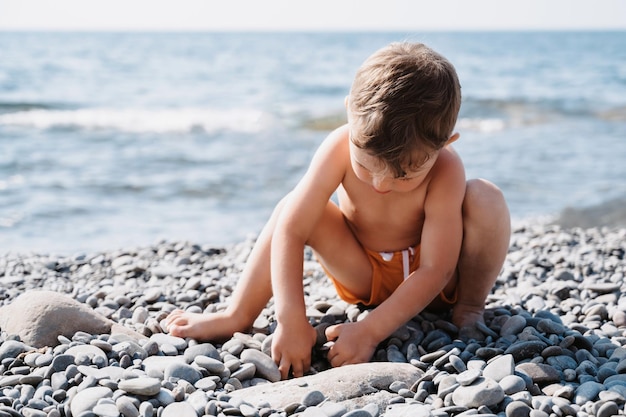 かわいい男の子が海の小石で遊んでビーチでリラックスしています海岸での野外活動