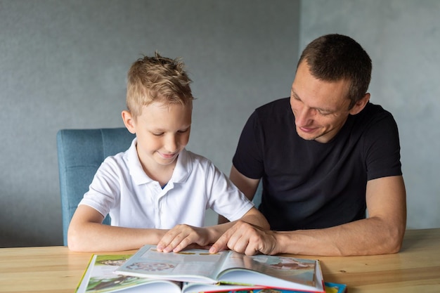 A cute boy is sitting at the table with his dad and watching a book about butterflies