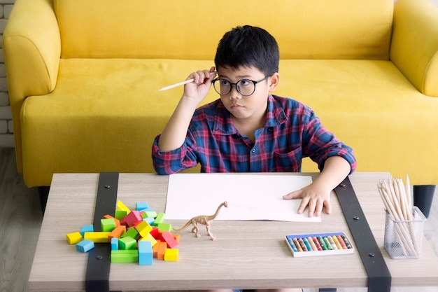 Photo the cute boy is thinking while doing his homework, sitting in the house.