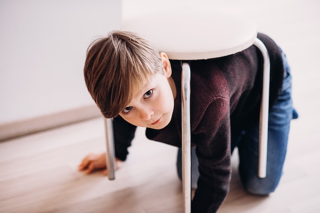 かわいい男の子の子供がカメのふりをして背中にスツールを持って床で遊ぶ