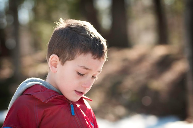 Cute boy looking down in forest during winter