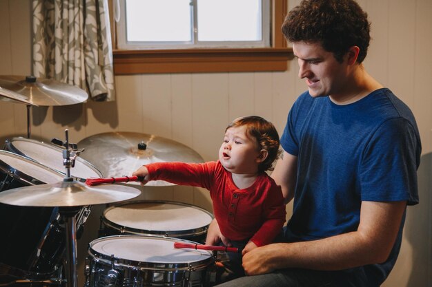 Photo cute boy playing drum while sitting with father at home