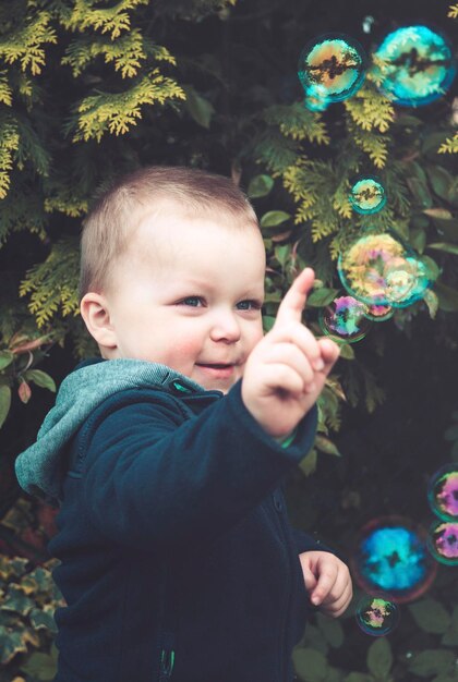 Photo cute boy playing with bubbles against plant