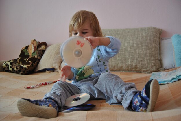Photo cute boy playing with compact discs on bed at home