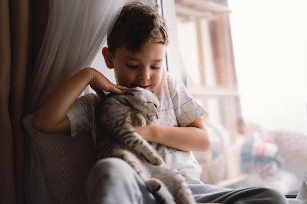 Cute boy playing with kitten sitting on the windowsill near the window cozy home