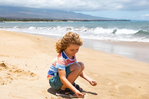 Cute boy playing with sand on summer tropical beach Happy kid sit on the seaside sandy beach and playing with sand