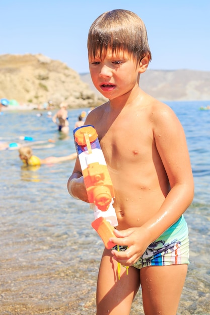 Фото Милый мальчик играет с водяным пистолетом, стоя в море