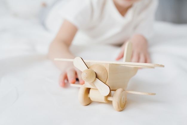 写真 ベッドの上に座っている木製の飛行機で遊ぶかわいい男の子