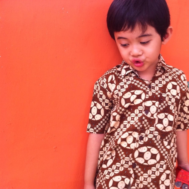 Photo cute boy puckering against orange wall