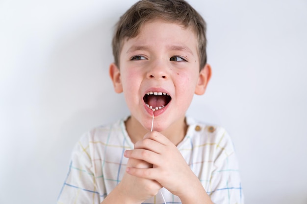 Cute boy pulling loose tooth using a dental floss. The boy's first milk tooth is loose. Toothache. Process of removing a baby tooth. Emotions of a child