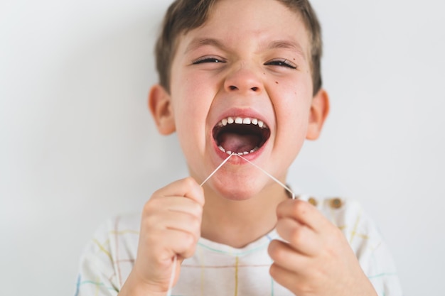 Cute boy pulling loose tooth using a dental floss process of removing a baby tooth