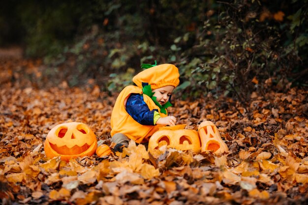 Cute boy in pumpkin costume among carved pumpkins