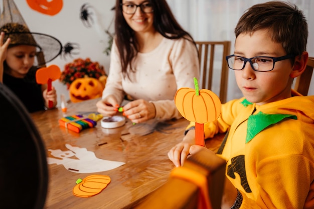 カボチャの衣装を着たかわいい男の子は、彼の手作りの紙のカボチャを示しています